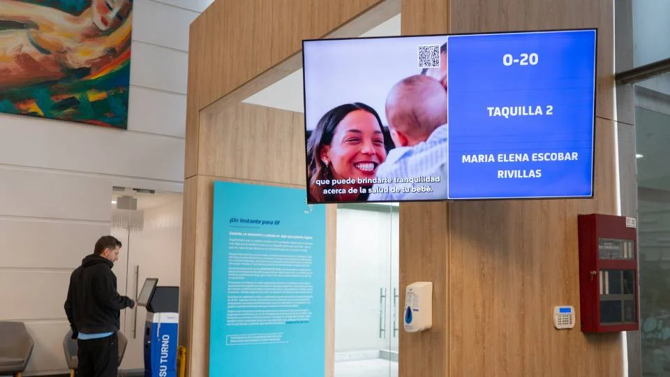 Tela de chamada de senhas combinada com sinalização digital reproduzindo vídeo corporativo em sala de espera